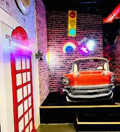Themed room with vintage red car, brick wall, neon signs, and British phone booth